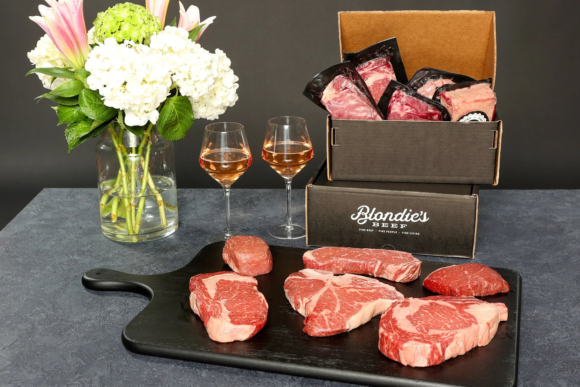 Blondie’s Beef Black Level Box showcasing assorted Wagyu cuts on a cutting board with branded packaging, wine glasses, and flowers.